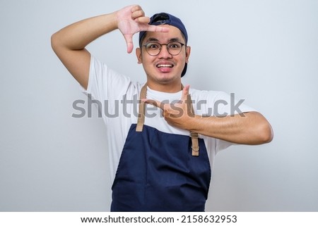 Young asian delivery man wearing glasses and cap isolated white background smiling making frame with hands and fingers with happy face