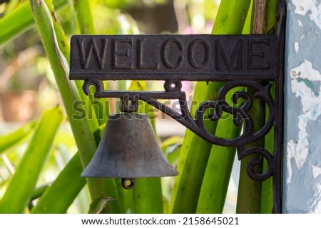 A closeup of a welcome sign with a hanging bell