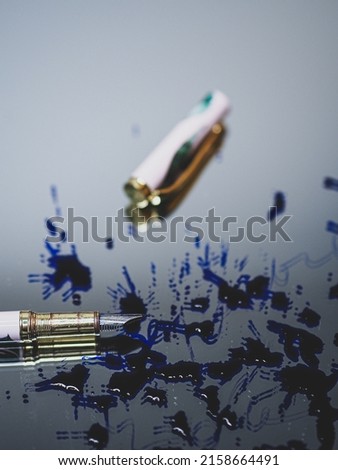 A vertical selective focus shot of a pen with its cover beside it and blue ink splashed, on a mirror table