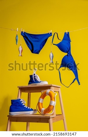 A blue swimsuit and wooden fish hang on a rope on a yellow background and blue sneakers with a lifebuoy stand on the stairs