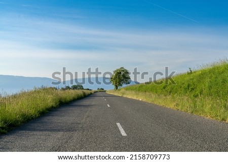 An empty blacktop highway in the countryside leading through green grass meadows to mountains in the background Royalty-Free Stock Photo #2158709773