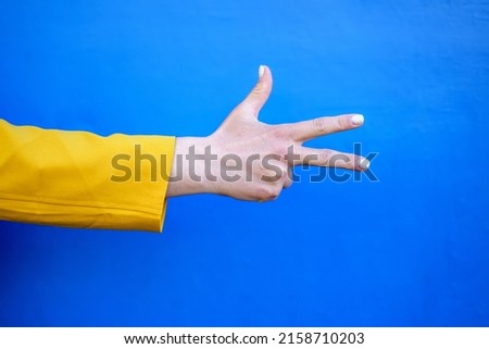 a hand in a yellow sleeve shows three fingers on a blue background. Royalty-Free Stock Photo #2158710203