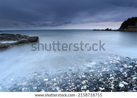A beautiful landscape view of stony beach by majestic sea water and a blue sky on the horizon Royalty-Free Stock Photo #2158718755