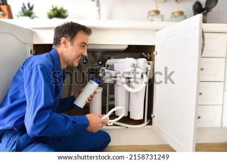 Technician installing reverse osmosis equipment under the sink. Front view. Horizontal composition. Royalty-Free Stock Photo #2158731249