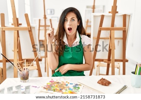 Beautiful caucasian woman at art studio pointing finger up with successful idea. exited and happy. number one. 