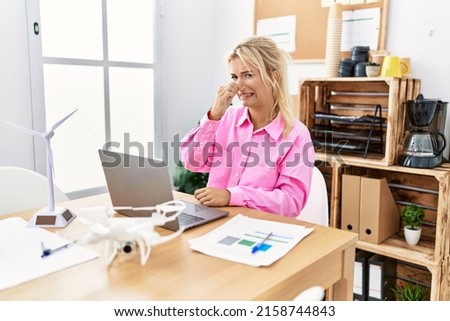 Young caucasian woman working at the office smelling something stinky and disgusting, intolerable smell, holding breath with fingers on nose. bad smell  Royalty-Free Stock Photo #2158744843