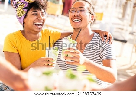 Happy young people toasting mojito drinks at beach cocktail bar -  friends having fun together drinking on happy hour at open air pub restaurant - Youth and summertime concept