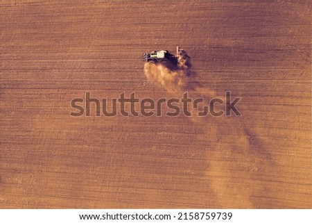 Farmer in a Tractor preparing a field with a seedbed cultivator, Pre seeding activities in early spring season of agricultural works at farmlands. Dry season with draught. Top down view. Royalty-Free Stock Photo #2158759739