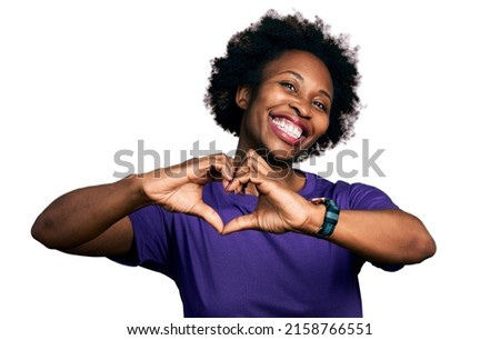 African american woman with afro hair wearing casual purple t shirt smiling in love doing heart symbol shape with hands. romantic concept. 