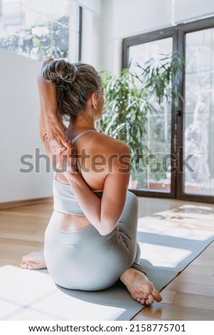 Rear view of fit woman doing gomukhasana at home. Fitness female holding hands behind back and stretching. Grey-haired senior lady is engaged in fitness, stretching, yoga Royalty-Free Stock Photo #2158775701