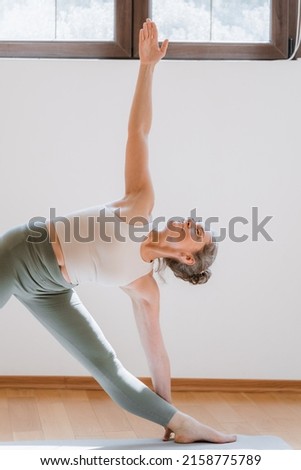 Full length view of the sporty mature woman practicing yoga, stretching in Revolved Downward Facing Dog exercise, working out at home Royalty-Free Stock Photo #2158775789