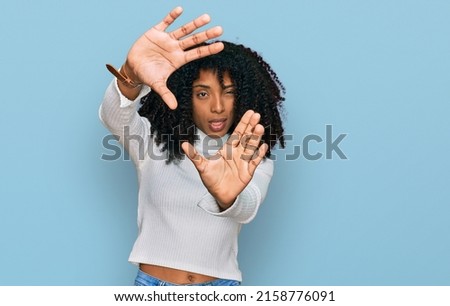 Young african american girl wearing casual clothes doing frame using hands palms and fingers, camera perspective 