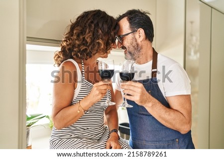 Middle age hispanic couple smiling confident toasting with wine at kitchen