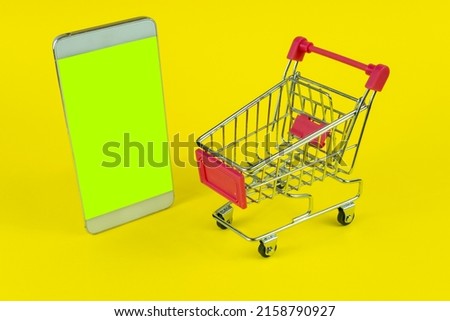 Mobile phone and supermarket trolley isolated on white background, e-commerce concept with copy space, online shopping from phone, sitting view, shopping cart idea, blank area