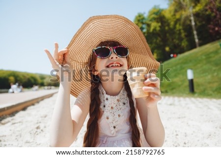 Charming little girl in a hat eats ice cream on the beach of the beach. Summer vacation concept.