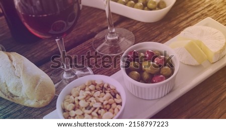 Image of wine glass filling with yellow liquid over table with wine and snacks. food, party and celebration concept digitally generated image.