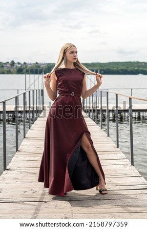 Beautiful woman stands wearing long dark red dress at nature. Travel concept.