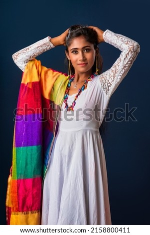 Portrait of a young beautiful girl wearing a white and colorful dress posing on grey background