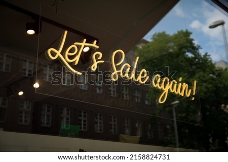 A selective focus shot of a yellow lightened letters let's sale again on a window with reflection
