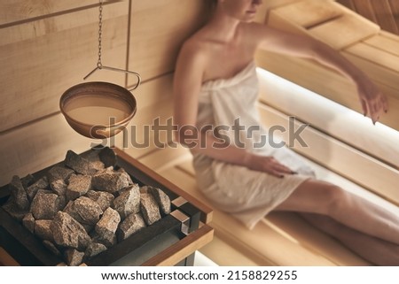 Woman relaxing in wellness spa, sweating in Finnish sauna, focus on sauna stove. Royalty-Free Stock Photo #2158829255