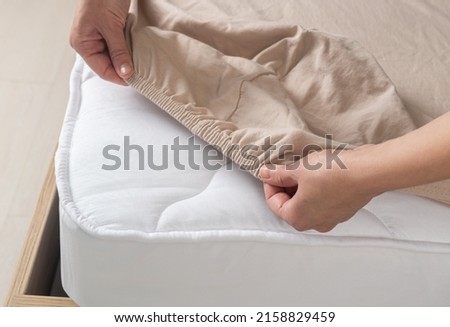 Woman puts beige sheets on the bed. Sheet on elastic band top view Royalty-Free Stock Photo #2158829459