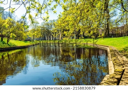 spring view on a river chanel in a green city park in may with young blooming salad shiny leafs on tree braches and reflection on water