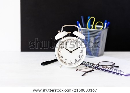 Time to return back to school or back to the office. White alarm clock, stationery. Glasses, black board on the background. High quality photo