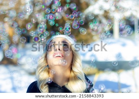 A smiling young caucasian woman looking up at soap bubbles background during a sunny winter day