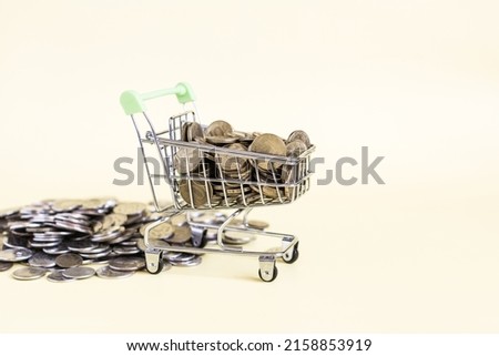 A grocery basket filled to the top with metal coins on a yellow background.