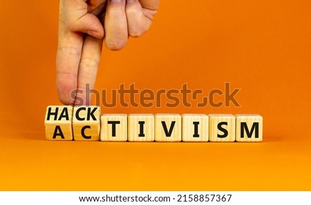 Activism or hacktivism symbol. Businessman turns wooden cubes and changes the word Activism to Hacktivism. Beautiful orange table orange background, copy space. Business activism hacktivism concept.