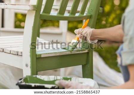 Painting Chair with brush in protective gloves. Worker paints garden furniture green. Renewing, Renovation Wooden Garden Furniture Royalty-Free Stock Photo #2158865437