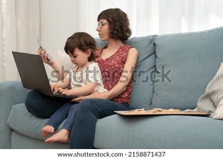 Mother and her daughter sitting on a sofa using a smart phone and a laptop. Addiction to computers, phones, gadgets, bad habit. 