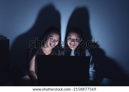 A vertical shot of two Hispanic Young women at a sleepover watching movies at dark on a laptop