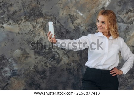 Portrait of smiling mature woman taking selfie on phone isolated on textured background. Successful businesswoman. Woman 50s