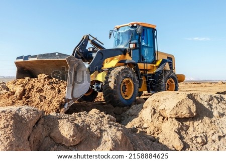 Bulldozer or loader moves the earth at the construction site against the blue sky. An earthmoving machine is leveling the site. Construction heavy equipment for earthworks Royalty-Free Stock Photo #2158884625