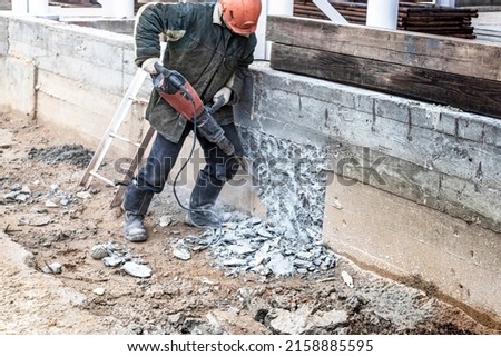 A worker with a jackhammer at a construction site levels a concrete wall. Powerful manual industrial equipment. Difficult construction job. Selective focus Royalty-Free Stock Photo #2158885595