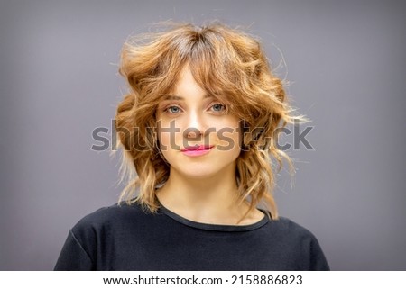 Portrait of a beautiful young caucasian red-haired woman with short wavy hairstyle smiling and looking at camera on dark gray background with copy space