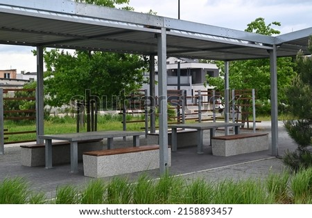 Recreation area with concrete tables and benches on a platform under a metal frame roof. play area,  Royalty-Free Stock Photo #2158893457