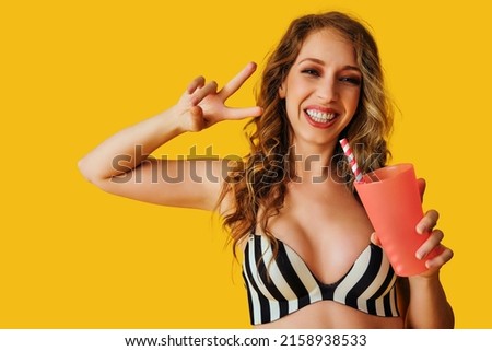 young adult beautiful woman smiling with soda and drink victory sign with hand on yellow background in summertime studio