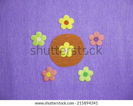 Symmetrical patterns of 5 colorful flowers on a blue crepe-paper background with a yellow flower at its center