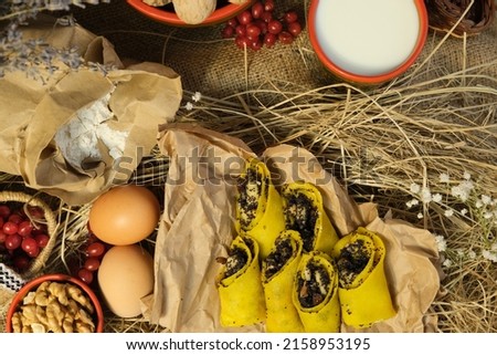 Pancakes, traditional Ukrainian slapjack with poppy seeds and walnuts. In red wooden utensils with Petrikovskaya painting. Craft eco paper. Maslenitsa, fried flapjack	 Royalty-Free Stock Photo #2158953195