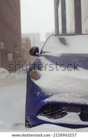A closeup vertical shot of a blue modern car covered by snow in the icy street in Montreal, Canada