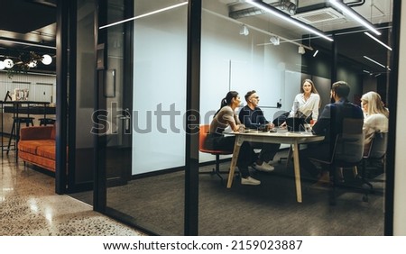 Team of diverse businesspeople having a meeting in a transparent boardroom. Group of business professionals having a discussion during a briefing. Colleagues collaborating on a new project. Royalty-Free Stock Photo #2159023887