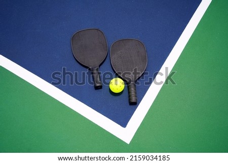 Two pickle ball paddles with a pickle ball on court.                           Royalty-Free Stock Photo #2159034185