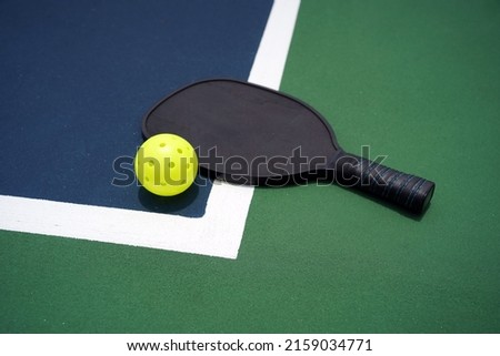 Pickle ball paddle with pickle ball on court.                               Royalty-Free Stock Photo #2159034771
