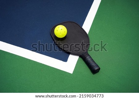Pickle ball paddle with pickle ball on court.                               Royalty-Free Stock Photo #2159034773