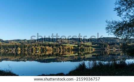 A blue boat sailing in the calm lake with the reflection of the colorful trees and sky in it autumn