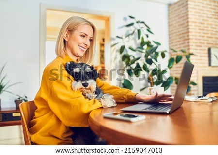 Smiling middle aged woman holding dog using laptop while at home office Royalty-Free Stock Photo #2159047013