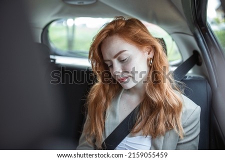 Beautiful young businesswoman sitting on back seat of a car and looking at mobile phone. Female business executive travelling by a cab.