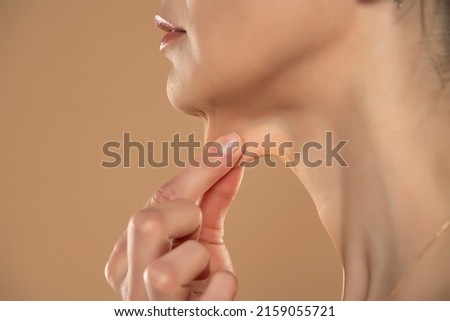 A close-up and side profile view of a caucasian lady pinching the loose skin at the front of her throat. Commonly called a turkey neck and corrected with a platysmaplasty. Royalty-Free Stock Photo #2159055721